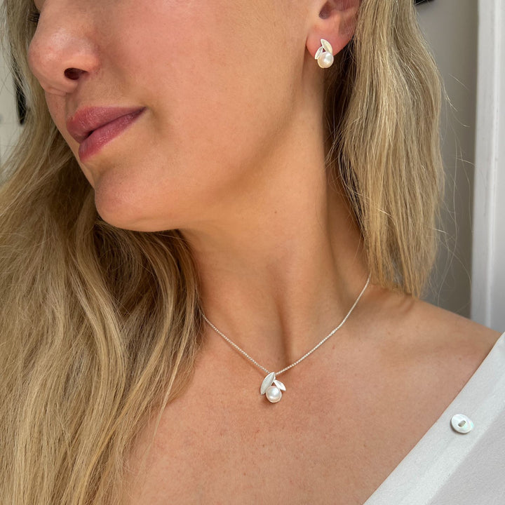 Close-up of a woman wearing a sterling silver necklace with a fresh water pearl and silver leaf pendant and matching earrings.