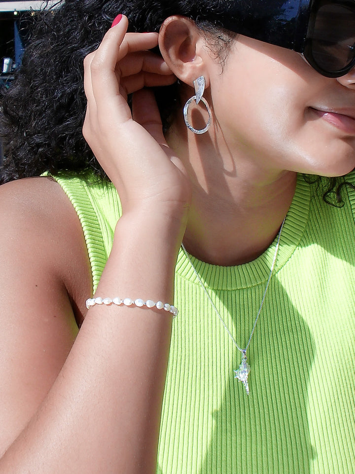 Close-up of a person wearing a silver hoop earring and pearl bracelet, with a green top.