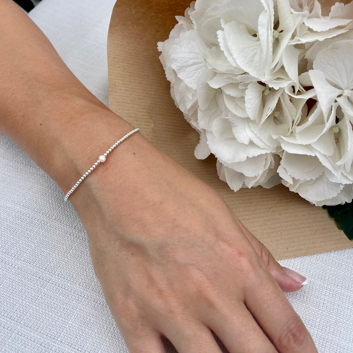 Hand wearing a bracelet with a bouquet of white flowers on a light surface