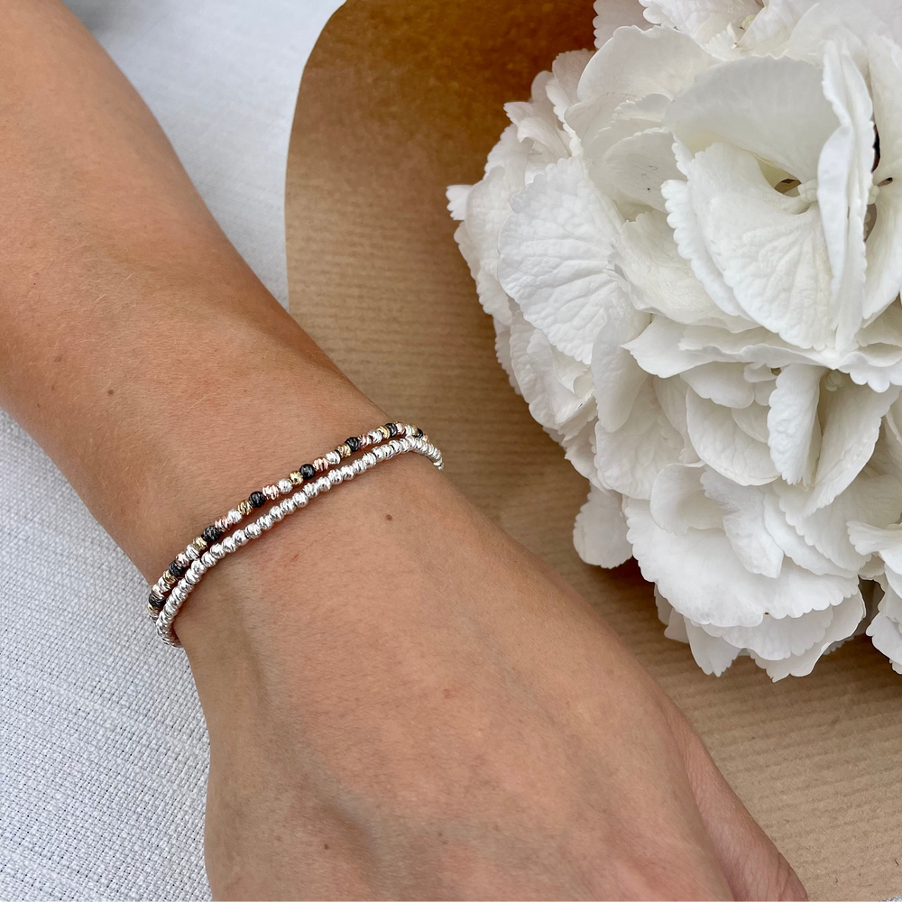Hand wearing a sparkly bracelet stack with white flowers in the background