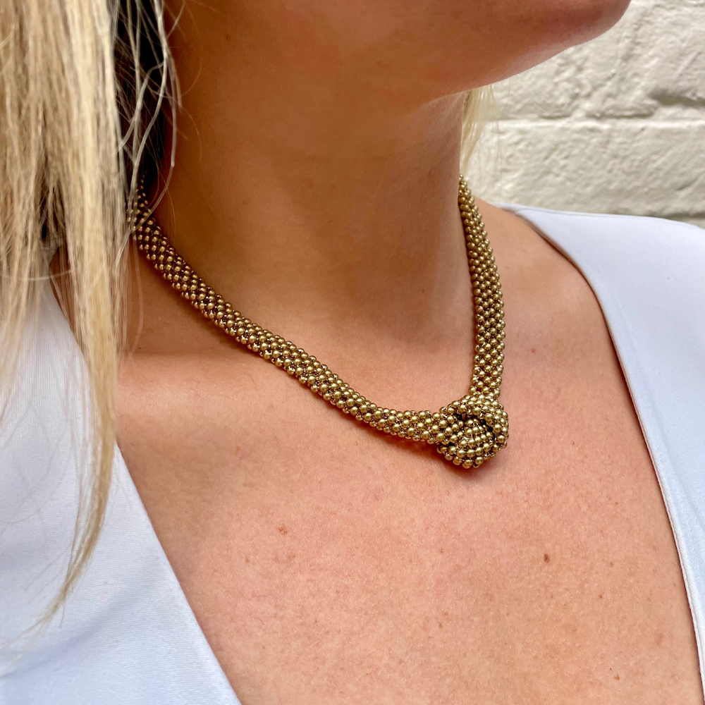 Gold mesh knotted necklace worn by a person with a white background