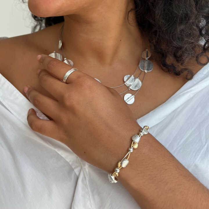 Close-up of a person wearing silver jewelry including a necklace, ring, and bracelet.
