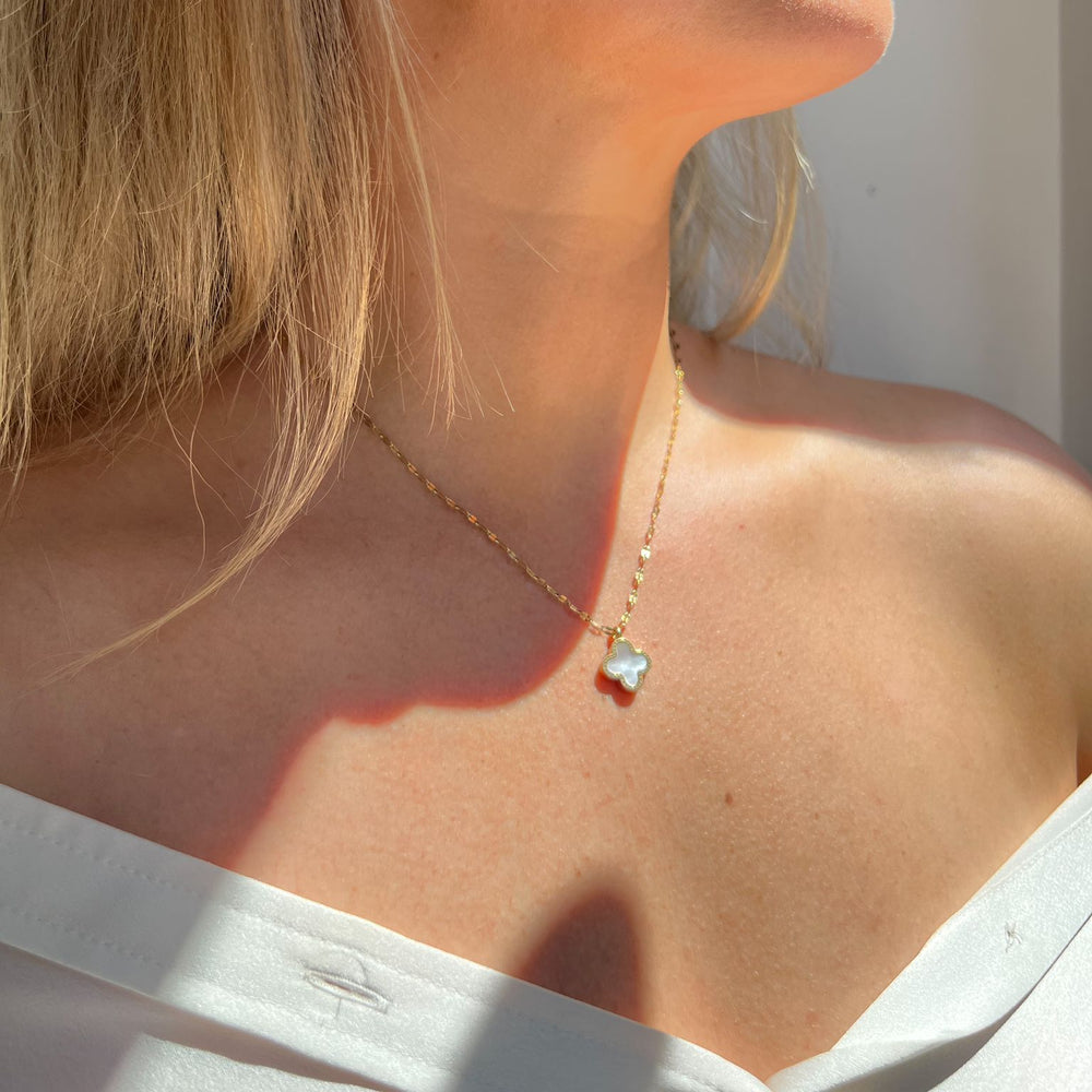 Close-up of a woman wearing a delicate necklace with a clover pendant.